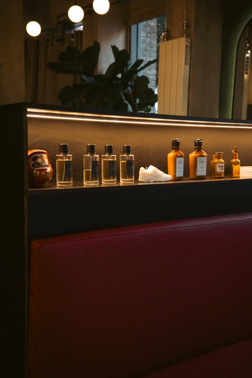 Verlichte richel boven de rode bank met parfumflesjes, Depot-flacons en een witte sneaker ertussen.